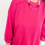 Person wearing a bright pink sweatshirt and blue jeans with a white background