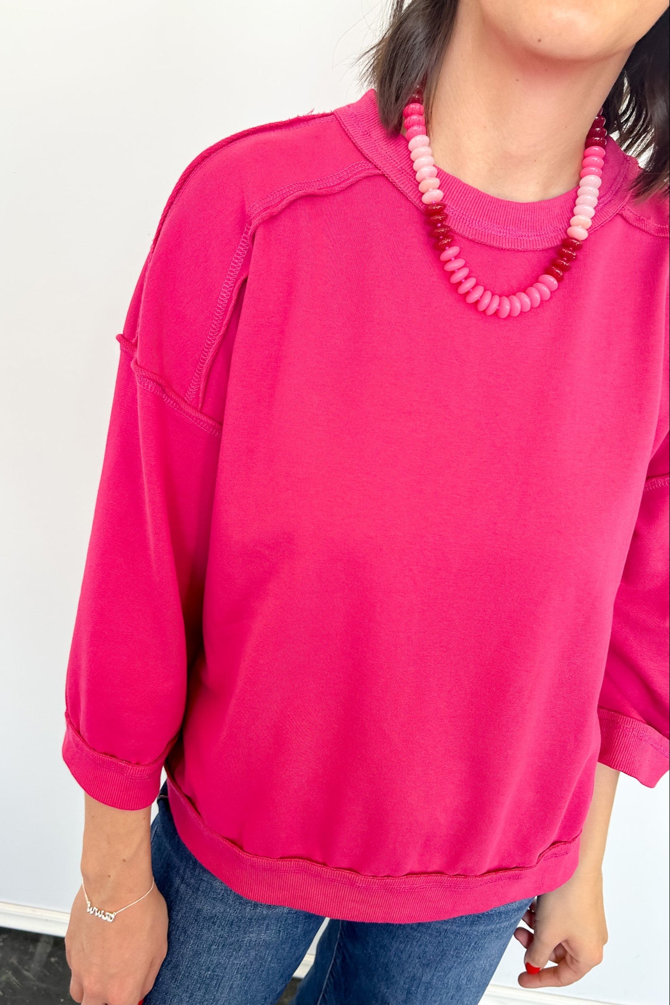 Person wearing a bright pink sweatshirt and blue jeans with a white background