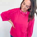 Woman wearing a bright pink sweatshirt and blue jeans against a white background