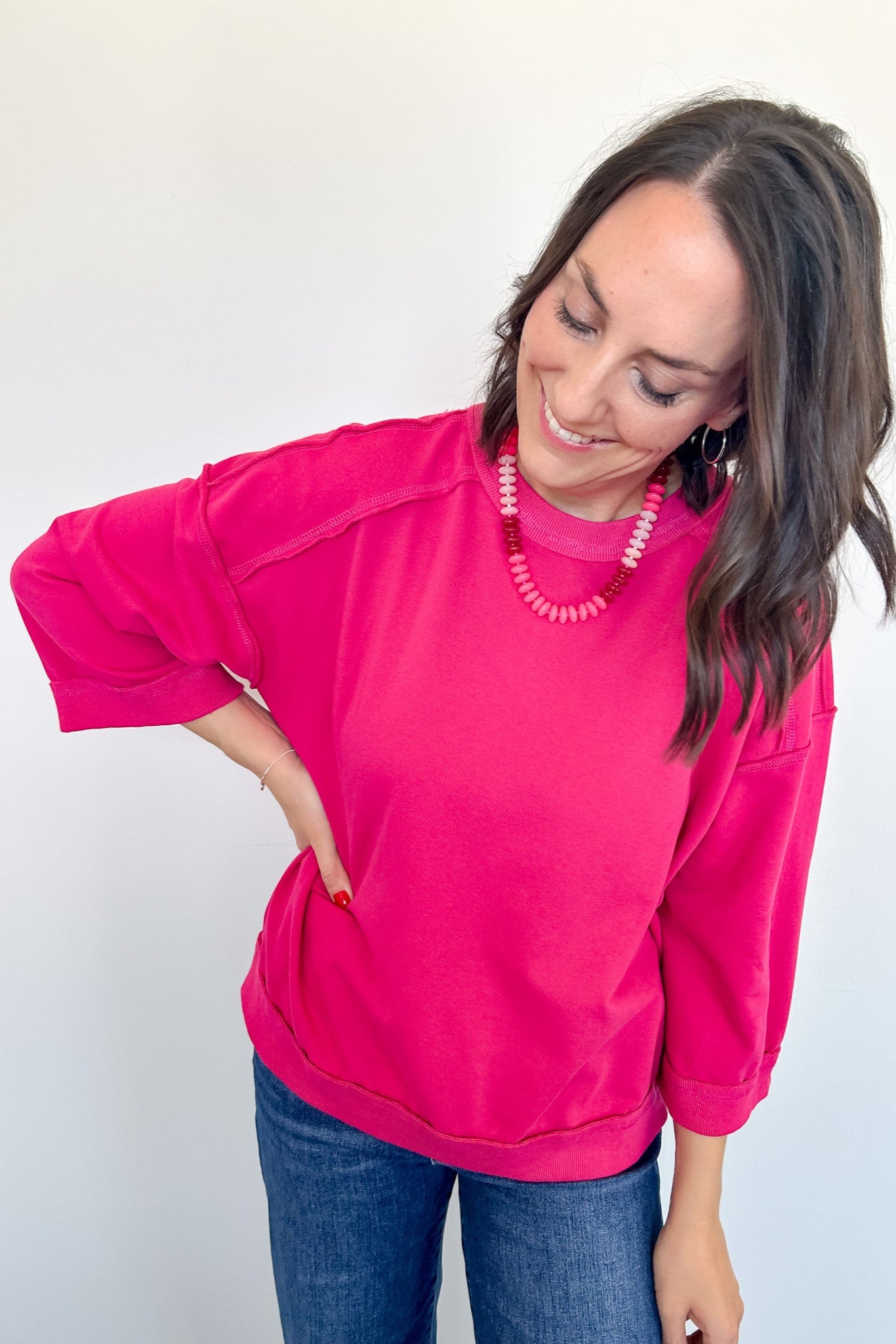 Woman wearing a bright pink sweatshirt and blue jeans against a white background