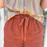 Person wearing a striped sleeveless top and rust-colored shorts standing in front of a door.