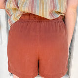 Person wearing rust-colored shorts and a striped shirt standing in front of a white door.