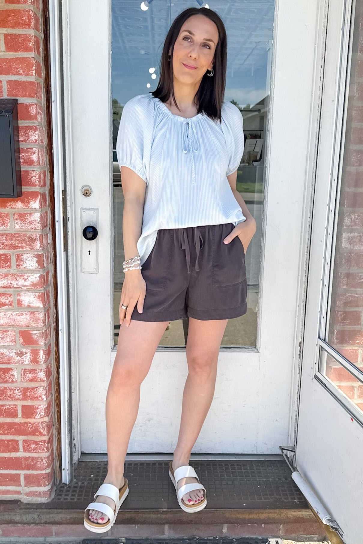 Woman standing in front of a door with a brick wall and glass door in the background