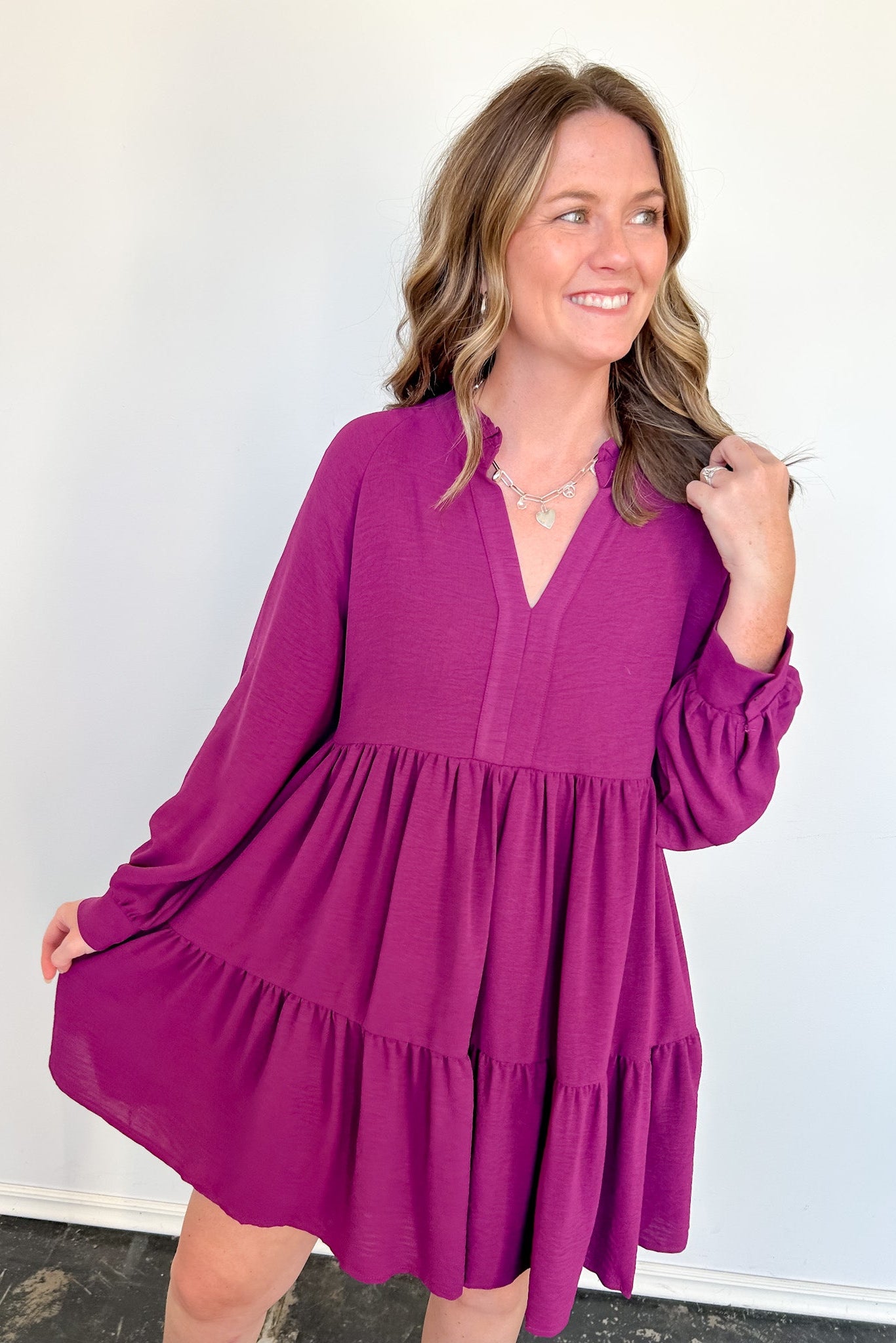 Woman wearing a short purple dress with long sleeves against a white wall.