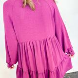 Person wearing a pink dress with long sleeves and ruffled layers against a white wall.
