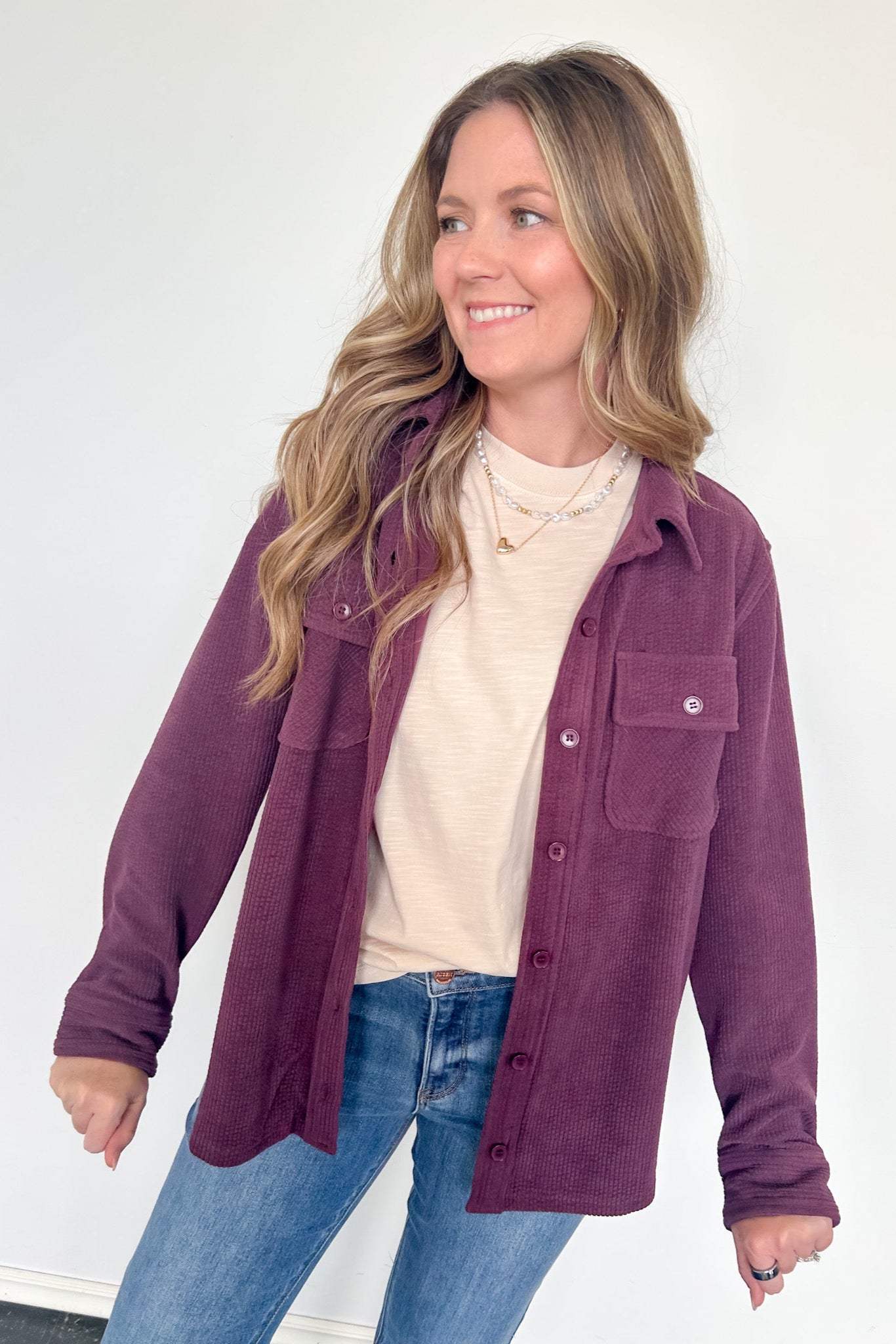Woman wearing a purple jacket over a white shirt and blue jeans on a white background