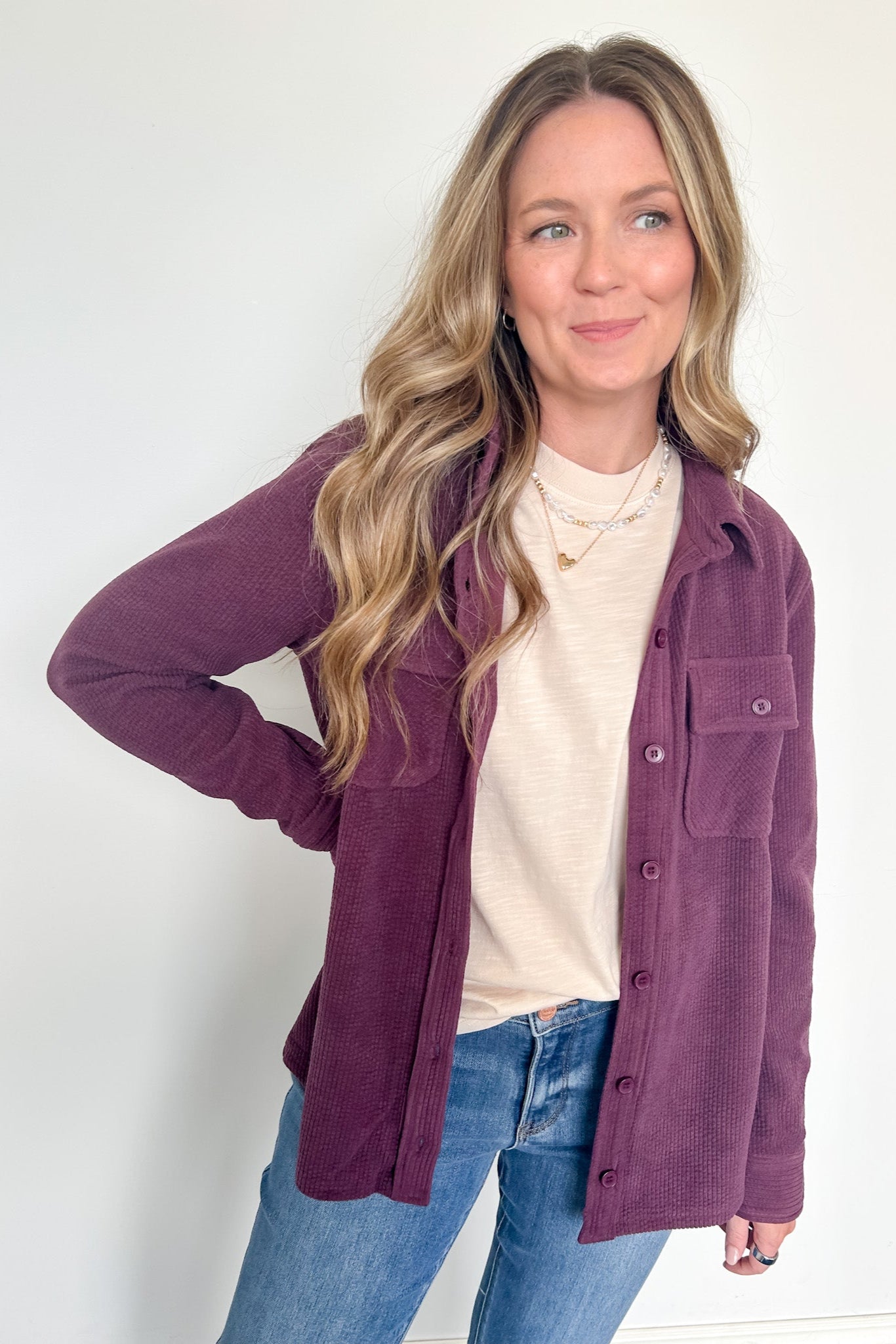 Woman wearing a purple jacket over a white shirt and blue jeans on a white background