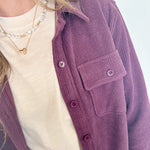 Person wearing a purple cardigan over a white shirt with a blurred background