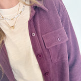 Person wearing a purple cardigan over a white shirt with a blurred background