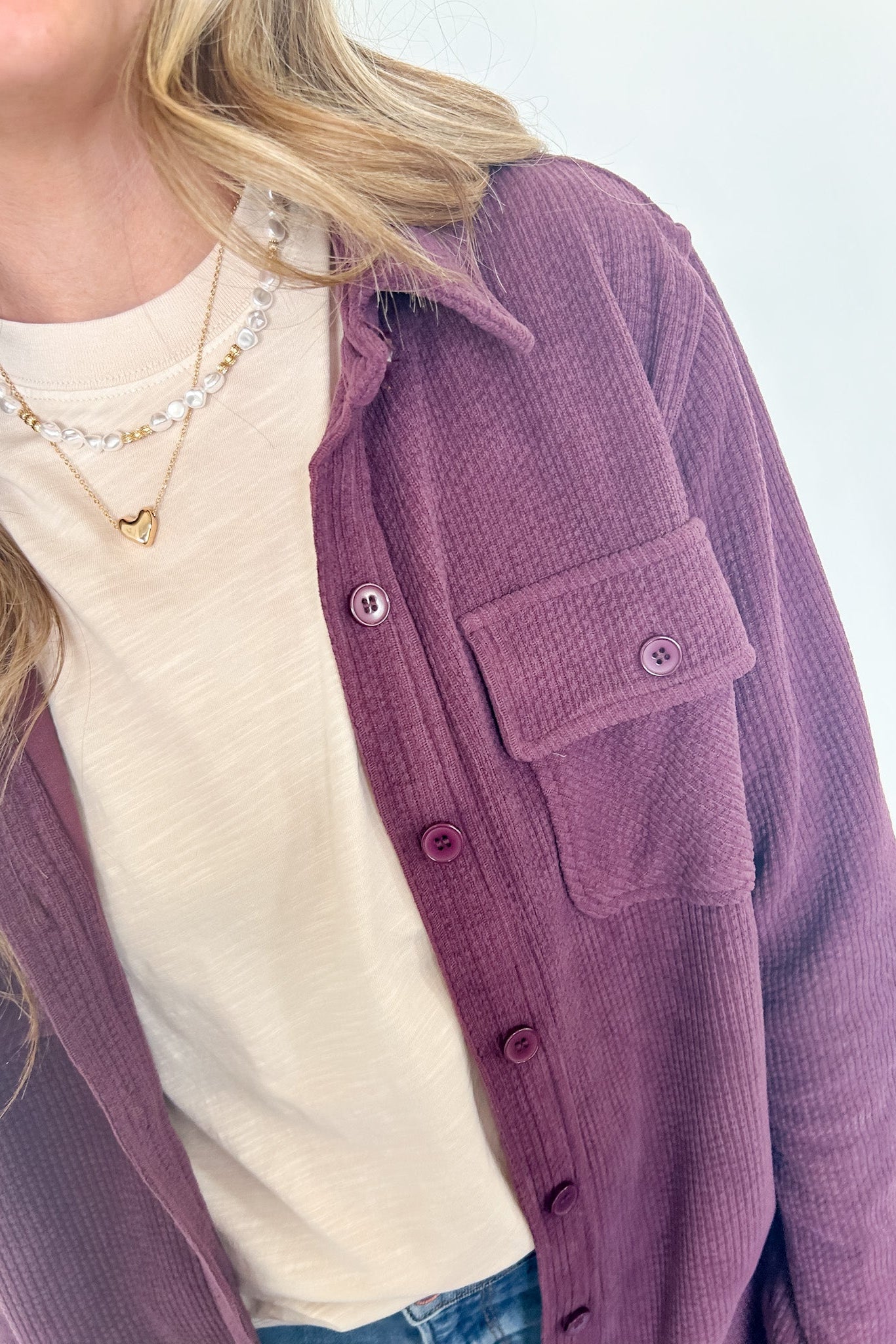 Person wearing a purple cardigan over a white shirt with a blurred background