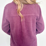 Person wearing a purple corduroy jacket with a white wall background
