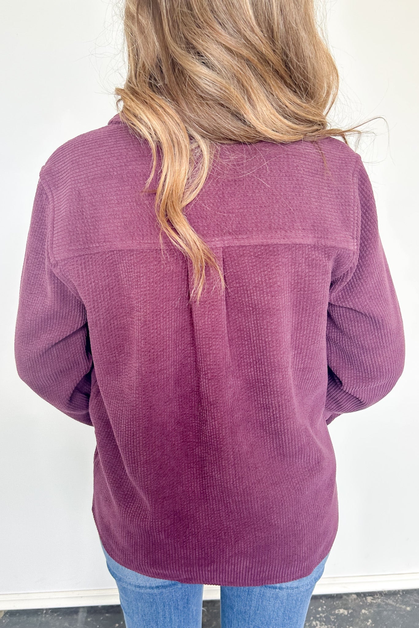 Person wearing a purple corduroy jacket with a white wall background