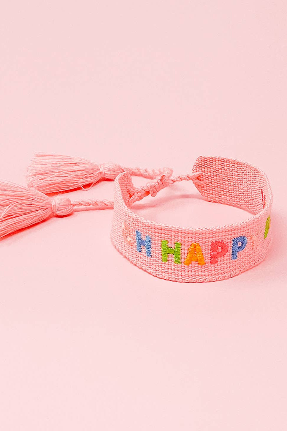 Pink woven bracelet with colorful letters spelling 'BE HAPPY' on a pink background