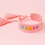 Pink woven bracelet with colorful letters spelling 'BE HAPPY' on a pink background