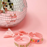 Pink bracelets with colorful text next to a disco ball on a pink background