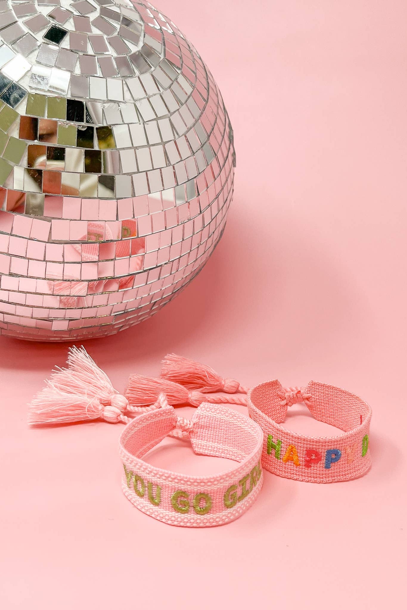 Pink bracelets with colorful text next to a disco ball on a pink background