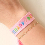 Pink woven bracelet with colorful letters on a wrist against a light background
