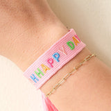 Pink woven bracelet with colorful letters on a wrist against a light background