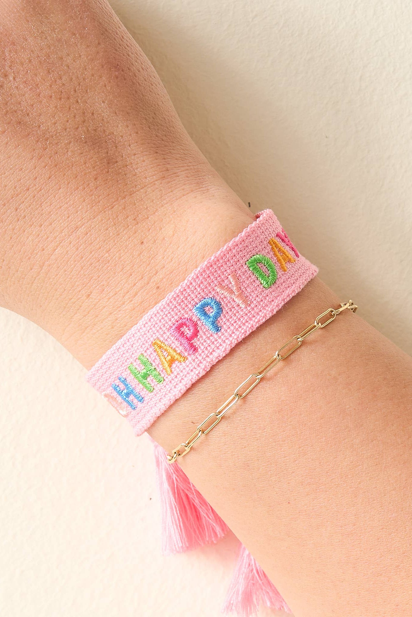 Pink woven bracelet with colorful letters on a wrist against a light background