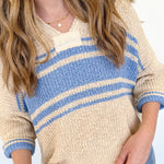 Person wearing a beige and blue striped sweater with jeans against a light background