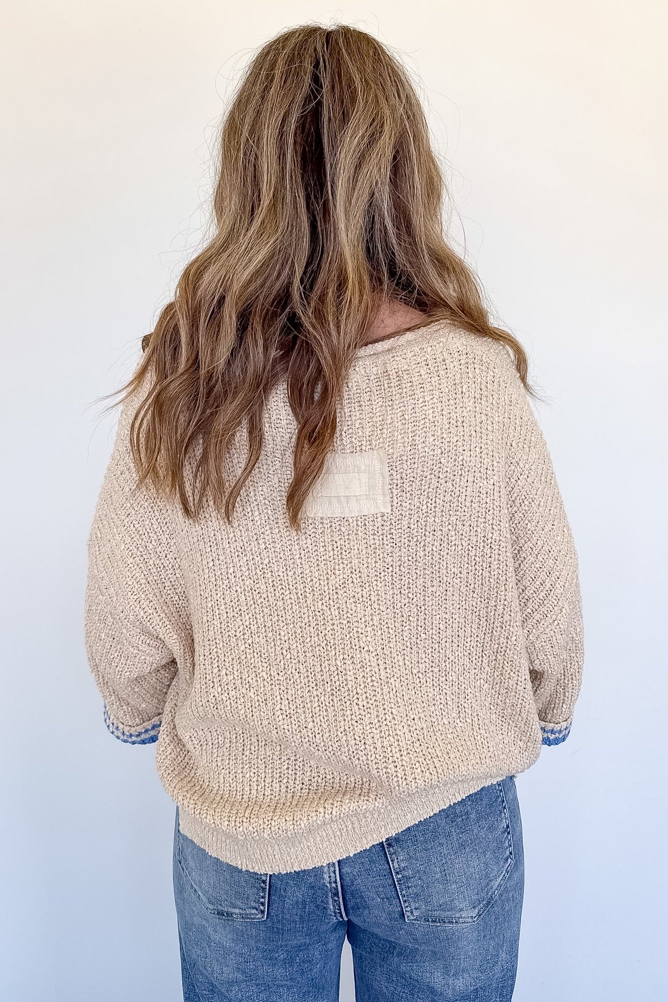 Person wearing a beige sweater with a pocket on a white background
