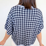 Person wearing a black and white checkered poncho against a plain background