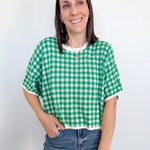 Woman wearing a green and white checkered shirt and blue jeans against a plain background