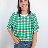 Woman wearing a green and white checkered shirt and blue jeans against a plain background