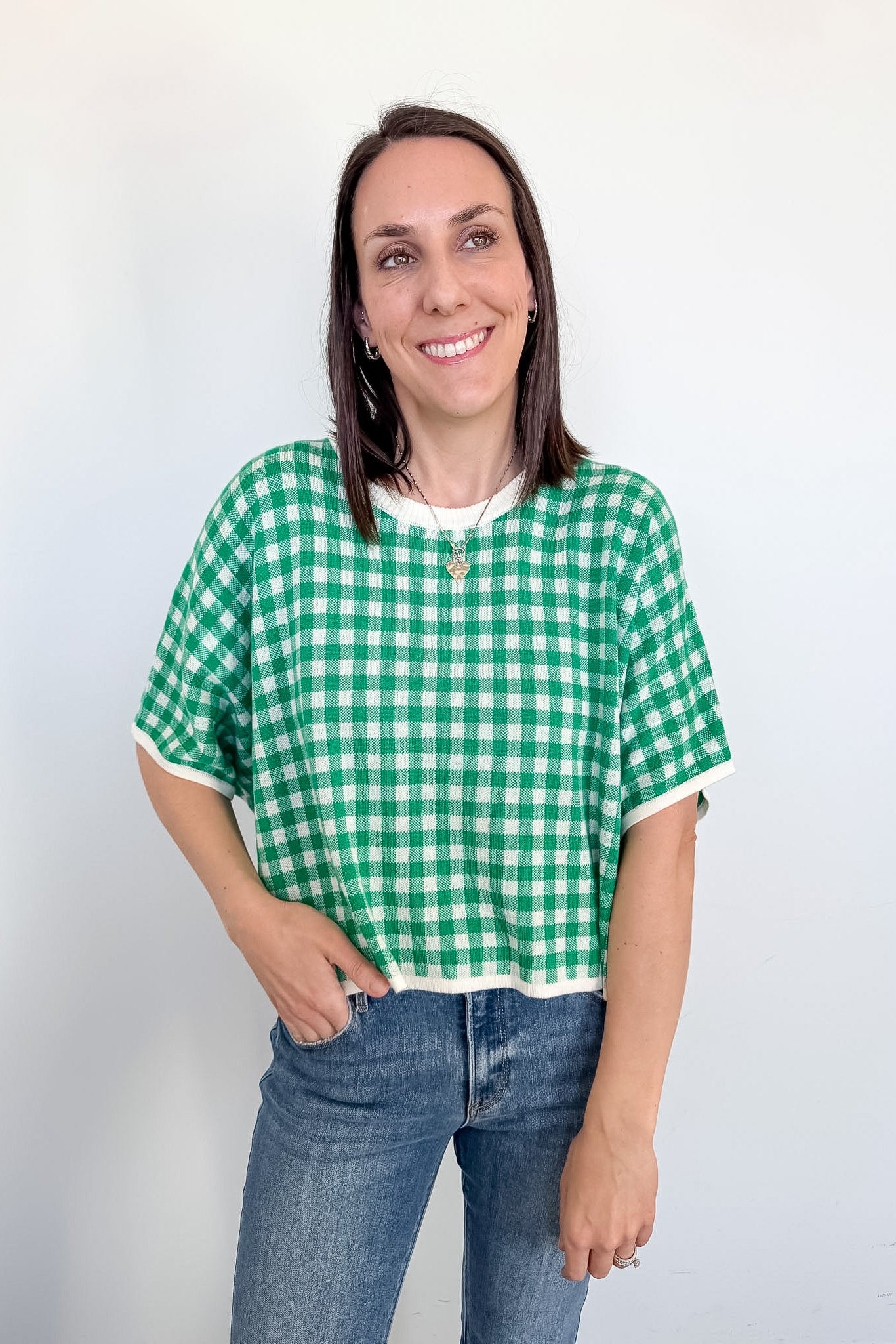 Woman wearing a green and white checkered shirt and blue jeans against a plain background