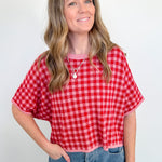 Woman wearing a red and white checkered shirt and blue jeans against a plain background
