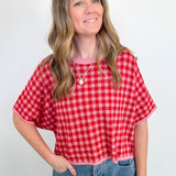 Woman wearing a red and white checkered shirt and blue jeans against a plain background