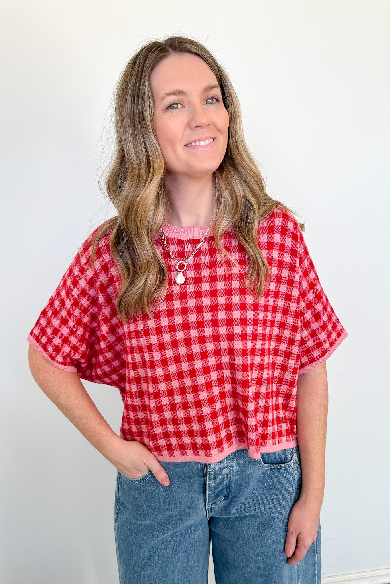 Woman wearing a red and white checkered shirt and blue jeans against a plain background