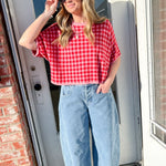 Woman wearing a red checkered shirt and blue jeans standing in front of a door.