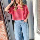 Woman wearing a red checkered shirt and blue jeans standing in front of a door.