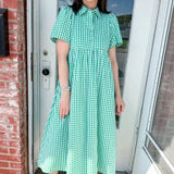 Woman in a green checkered dress standing outside a house.
