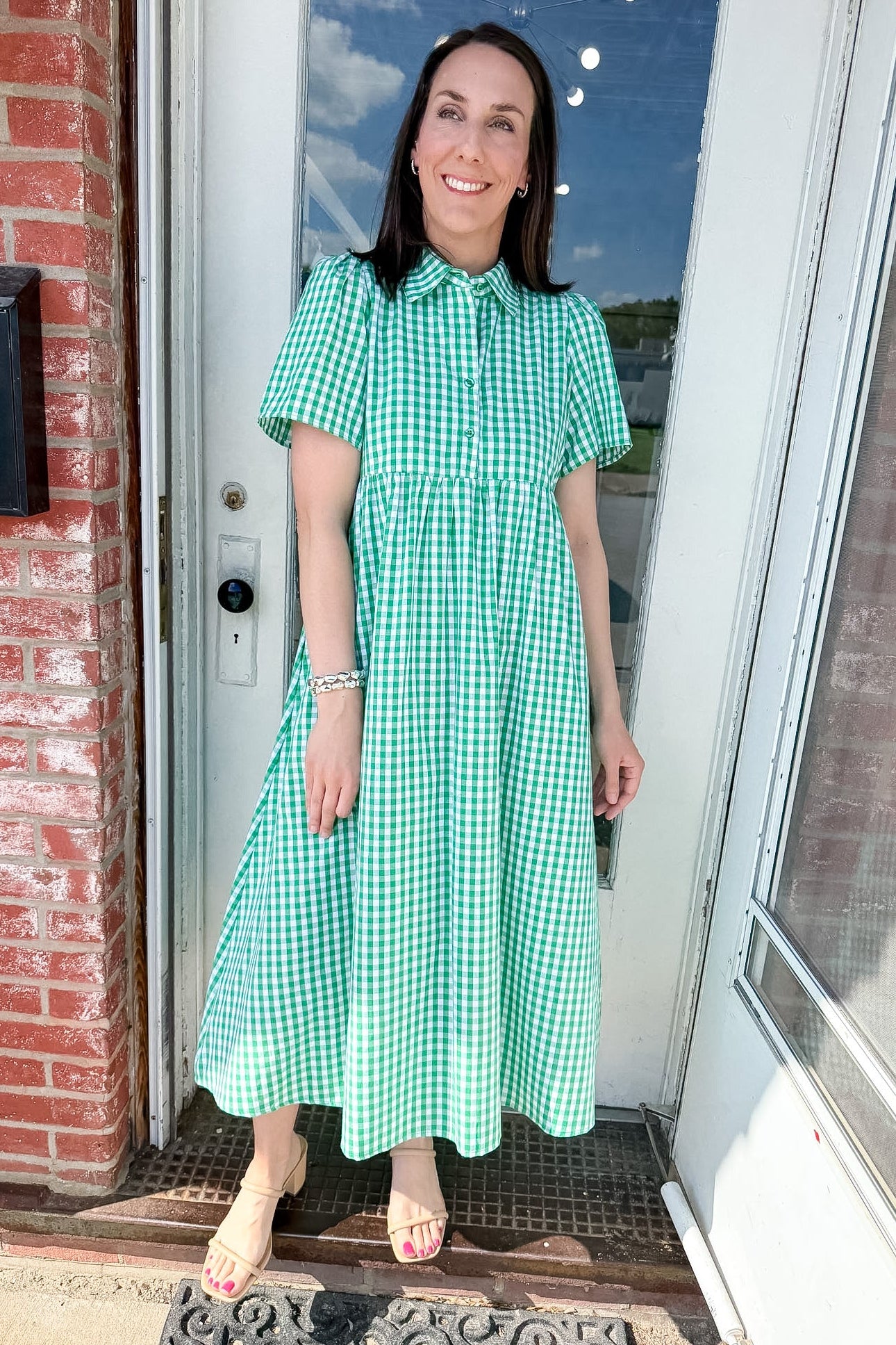 Woman in a green checkered dress standing outside a house.