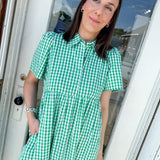 Woman wearing a green checkered dress standing in front of a door.