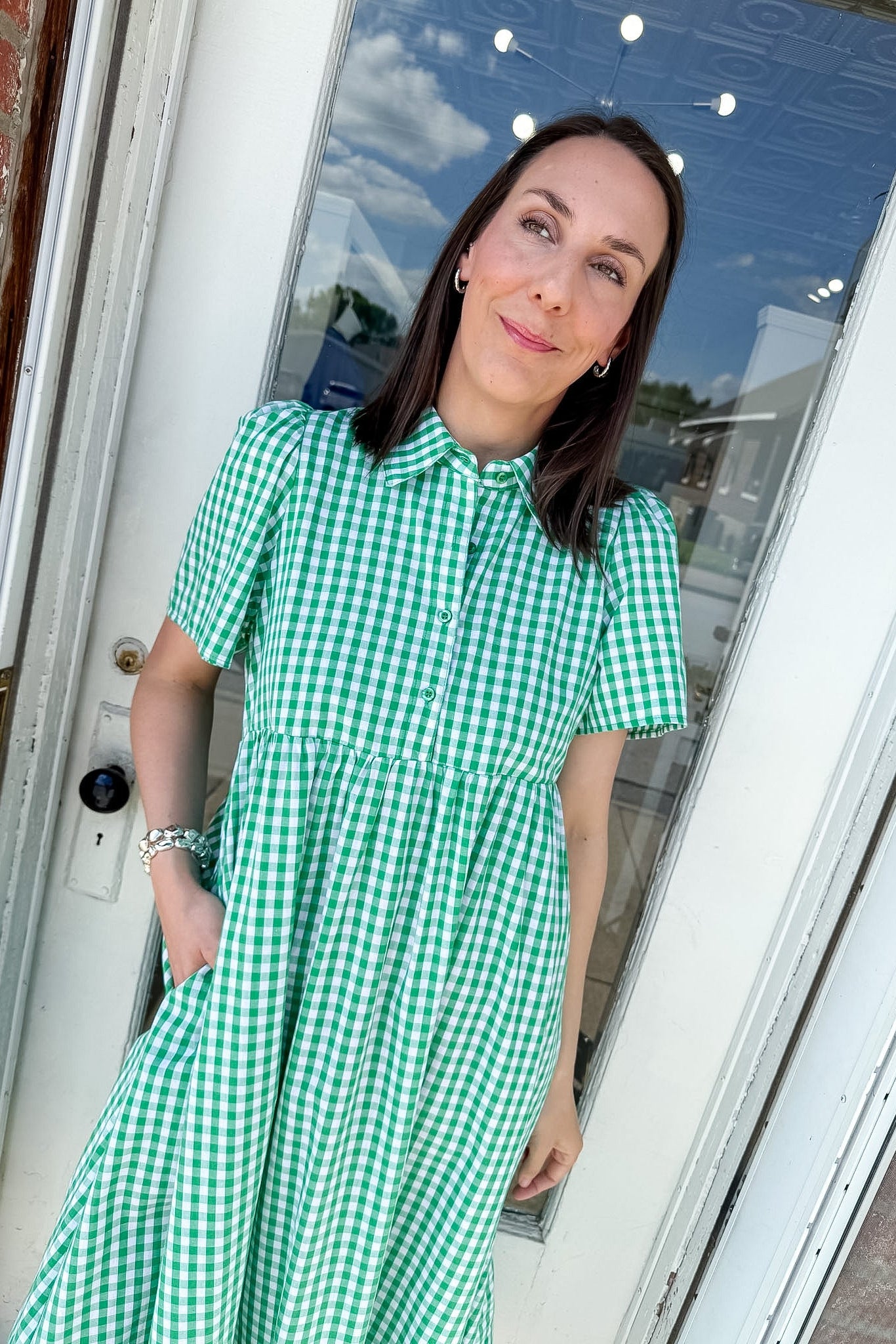Woman wearing a green checkered dress standing in front of a door.