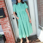 Woman in green dress with her hand in her pocket standing in front of a door.
