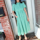 Woman in green dress with her hand in her pocket standing in front of a door.