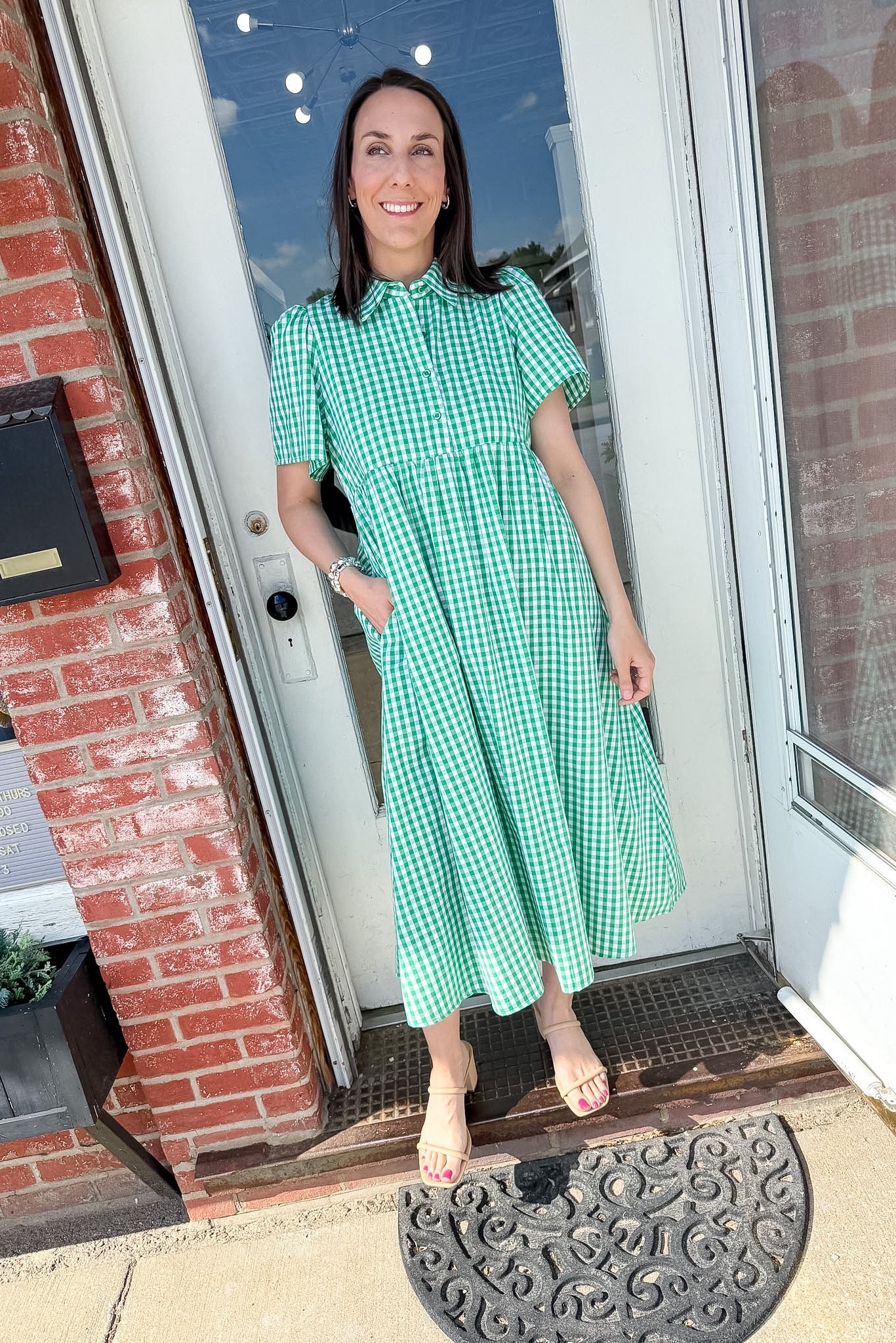 Woman in green dress with her hand in her pocket standing in front of a door.