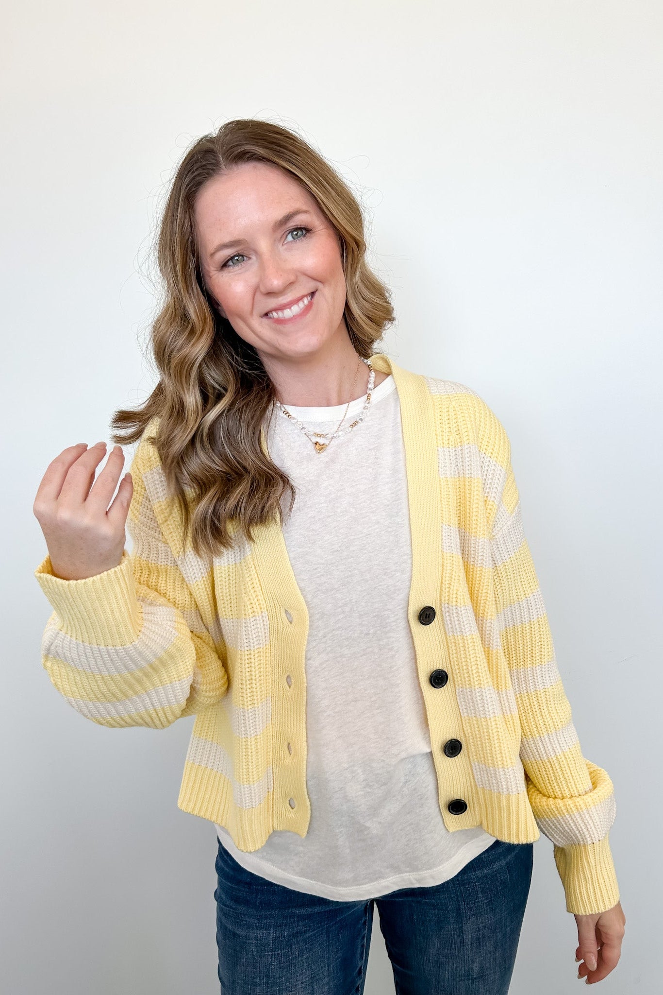 Woman wearing a yellow and white striped cardigan over a white shirt with a plain background