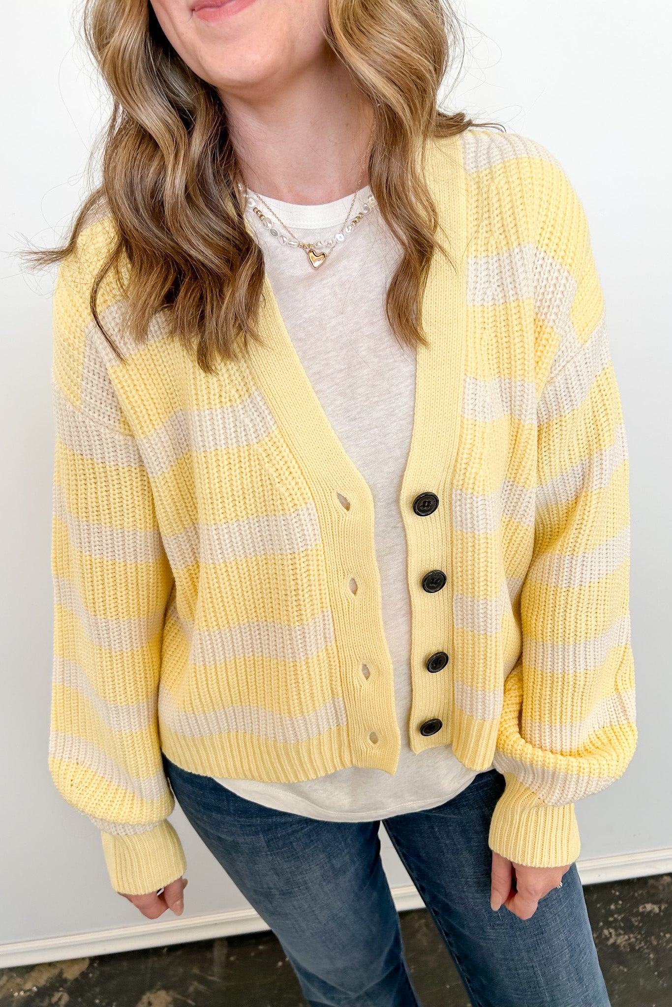 Person wearing a yellow and white striped cardigan over a white shirt and blue jeans against a white background