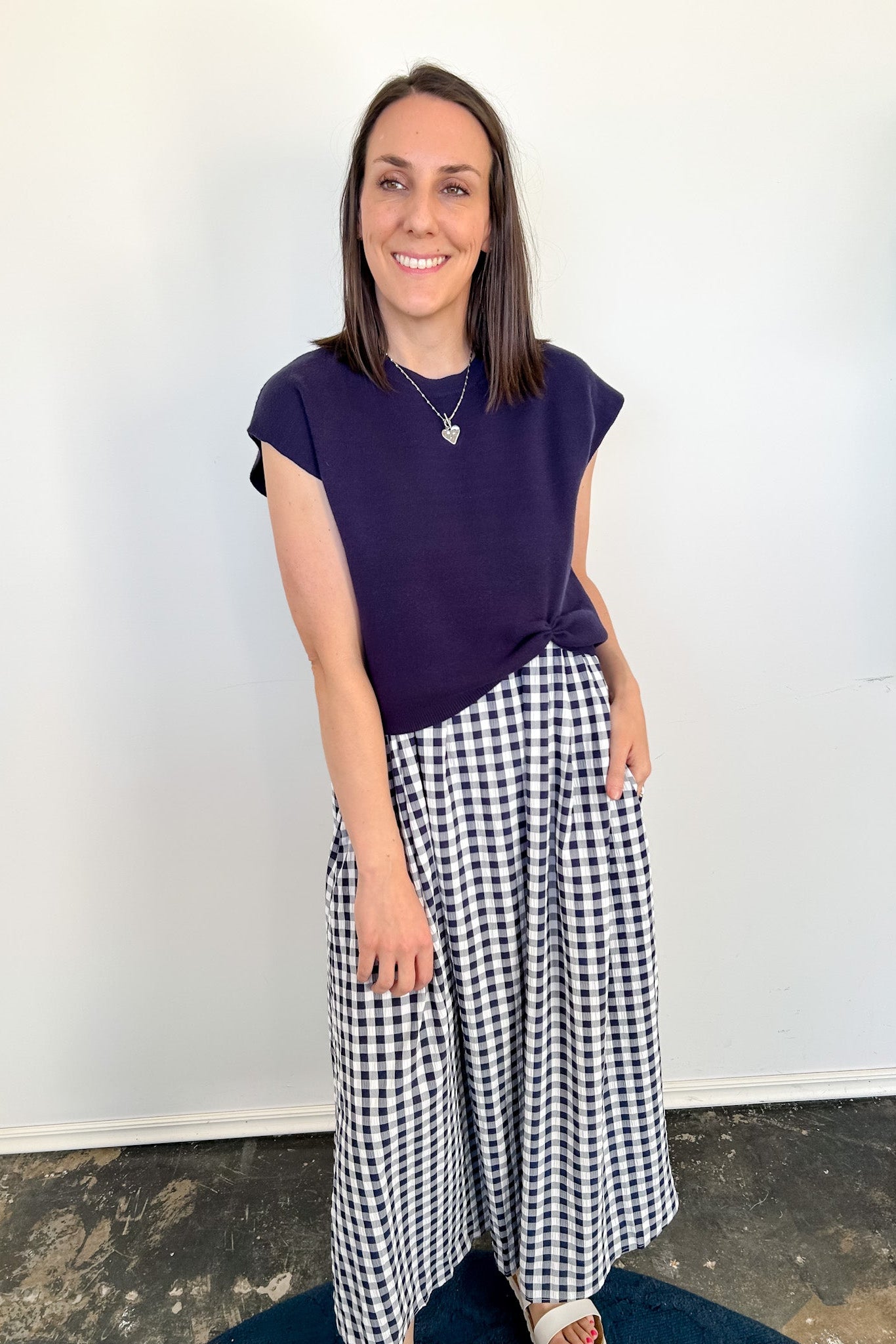 Woman wearing a purple top and black and white checkered skirt against a white wall.