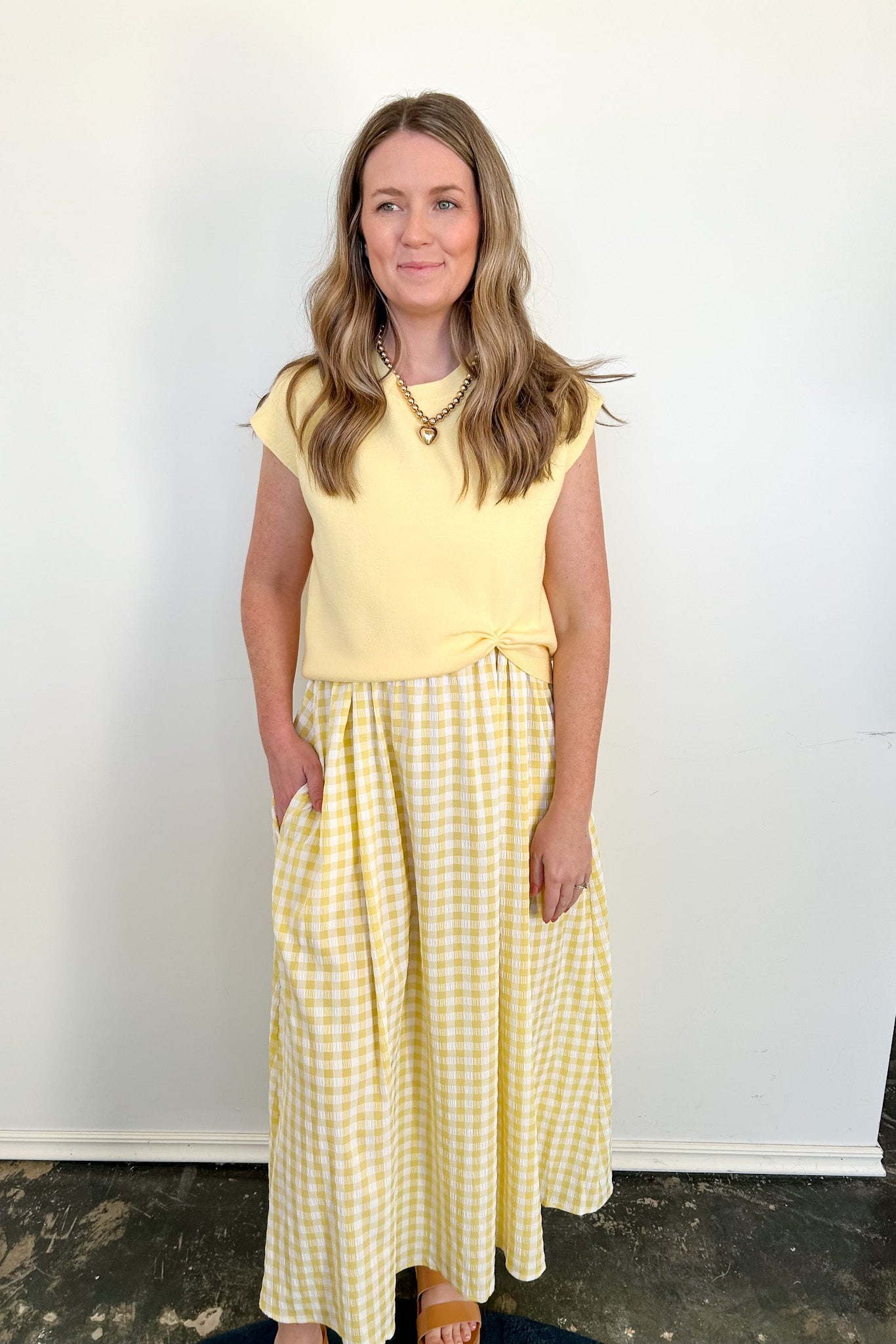Woman wearing a yellow top and checkered skirt against a white wall.