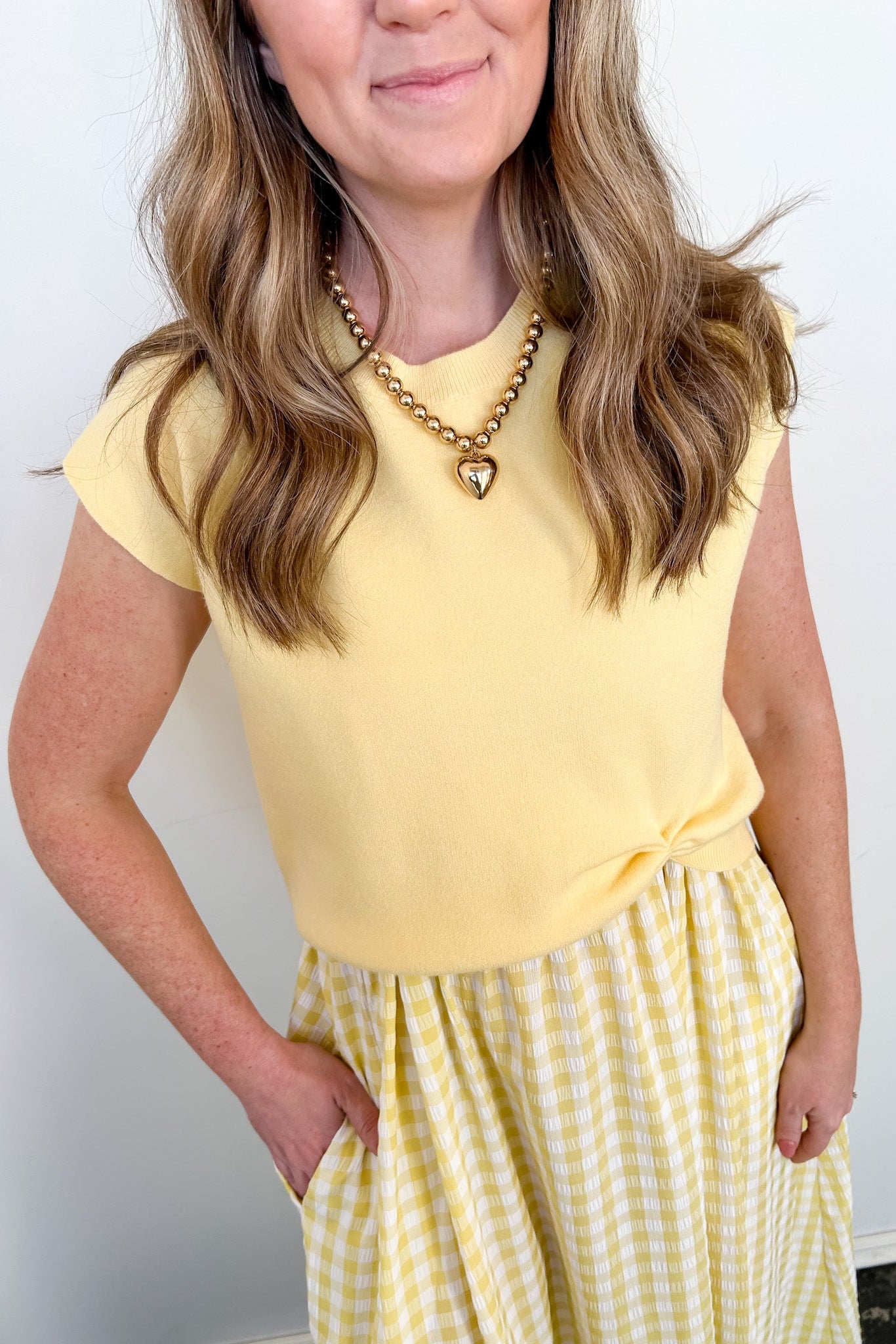Woman wearing a yellow top and checkered skirt against a white background