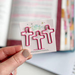 Hand holding a pack of pink paper clips with a branded label in front of a colorful notebook.