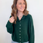 Woman wearing a green button-up shirt and light blue jeans against a white background