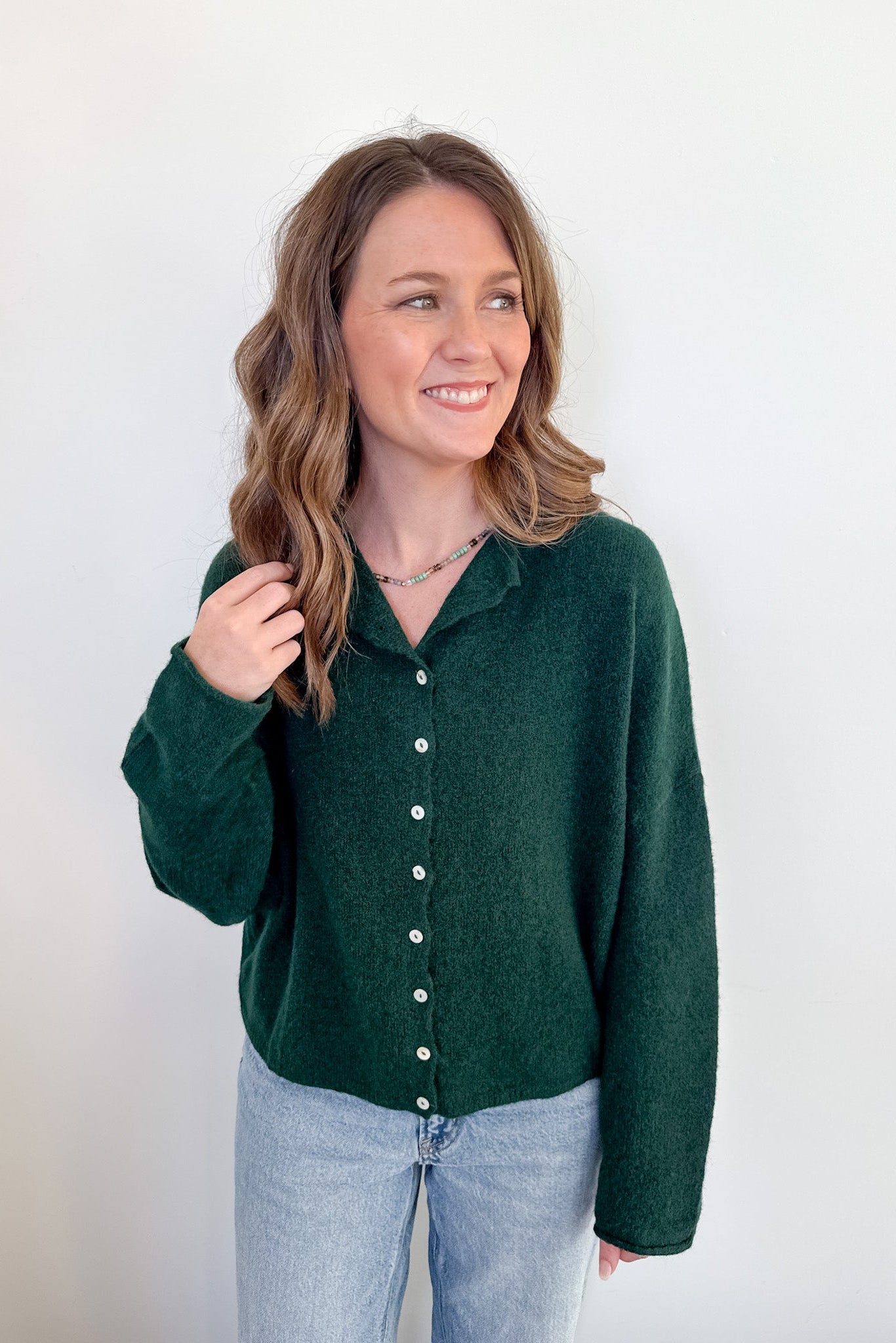 Woman wearing a green button-up shirt and light blue jeans against a white background