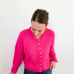 Person wearing a bright pink cardigan and blue jeans against a white background